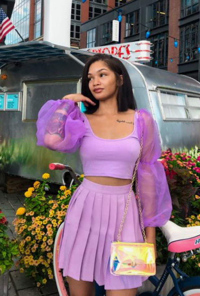 A woman wearing a lilac outfit with a yellow purse