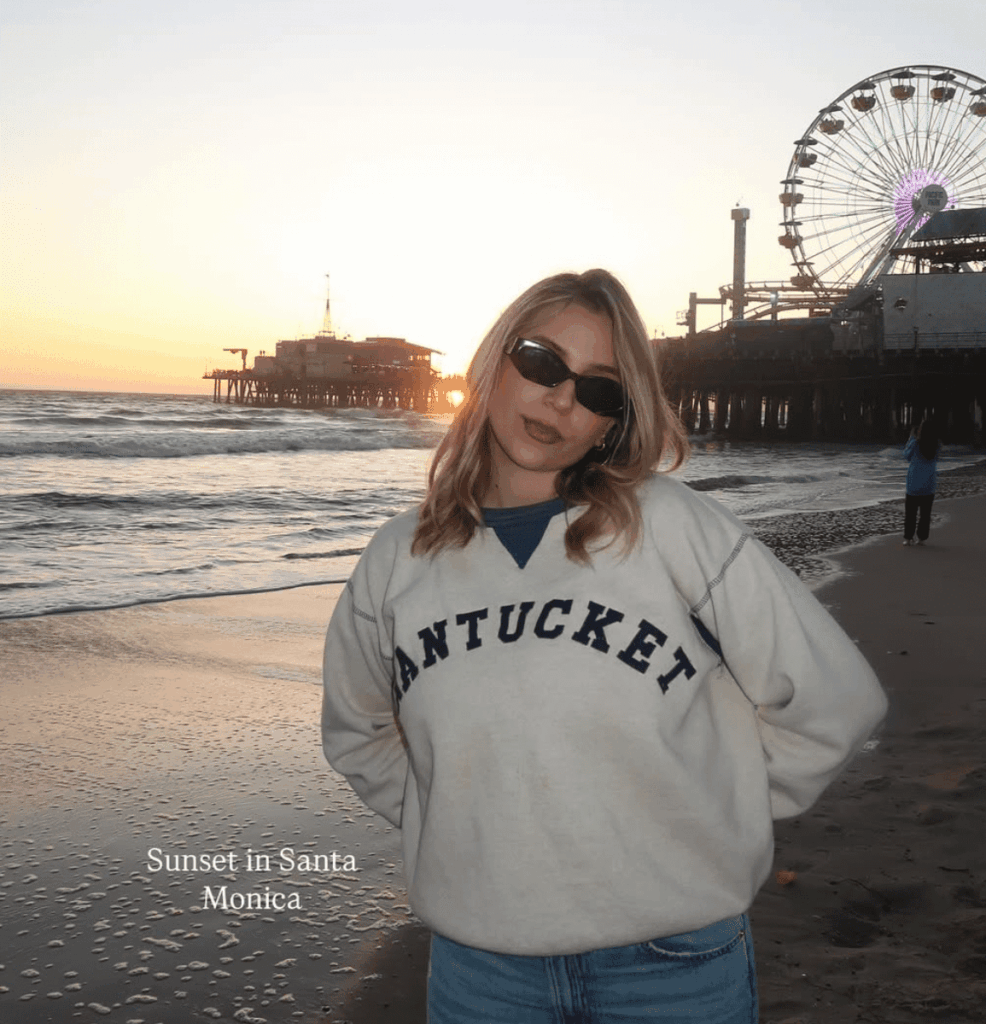 Lexy Silverstein wearing a white and navy blue "Nantucket" crewneck and jeans at the beach.